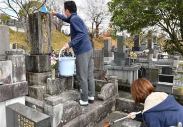 ひしゃくやほうきを手に墓を掃除する夫婦＝18日午後、熊本市中央区の立田山墓地