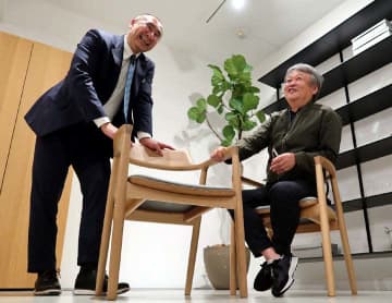 サミットで使われた椅子と同型の製品に手をかけ、思いを語り合う山中社長（左）と深沢さん