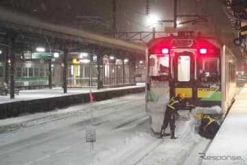 ニュース画像：北海道内は年末年始にかけて厳寒と大雪に見舞われたが、連休明けの1月11日は夜半にかけて再び大雪の予報が出ている。写真は2022年1月2日、函館本線小樽駅に停車中のH100形を除雪する社員。- 「大雪や強風で北日本各線を中心に運休や遅れ　1月11-12日の鉄道運行情報　」