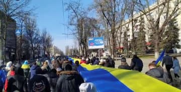 3月、ウクライナ南部ヘルソンで、国旗と同じ色の横断幕を運ぶデモ隊（ロイター＝共同）