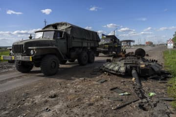 13日、ウクライナ・ハリコフ北部で、ロシア軍戦車の残骸のそばを通り過ぎるウクライナ軍車両（AP＝共同）