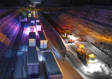 新名神高速道路で立ち往生するトラックの車列。右は除雪車＝25日午後6時43分、三重県四日市市