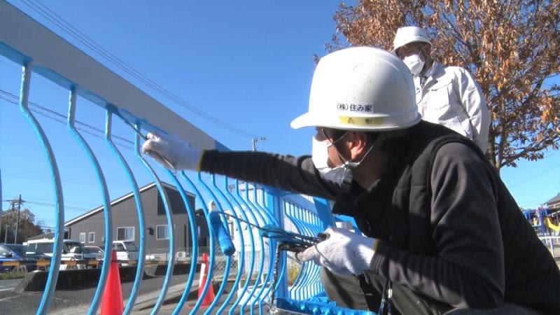 Volunteers paint the front gate of a children's center, and a "living house" comes forward
