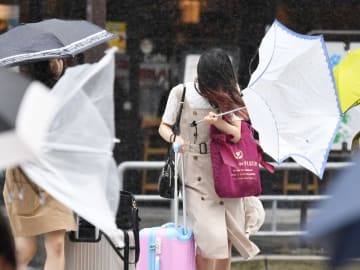 台風6号の接近で風雨が強まり、傘をあおられる歩行者=27日午前10時11分、名古屋市